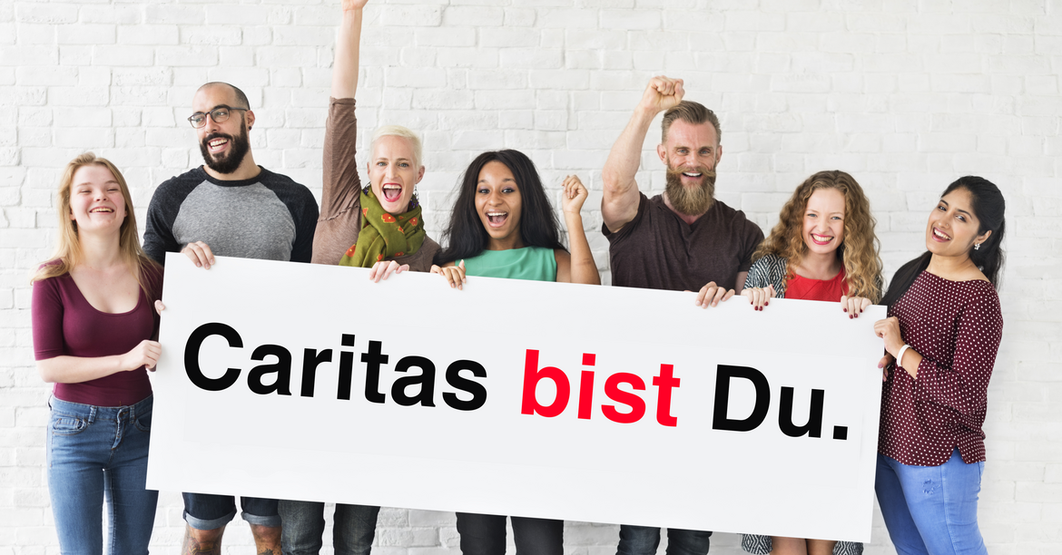 Eine Gruppe von Menschen stehen nebeneinander und halten ein Schild mit der Aufschrift "Caritas bist Du." in den Händen.