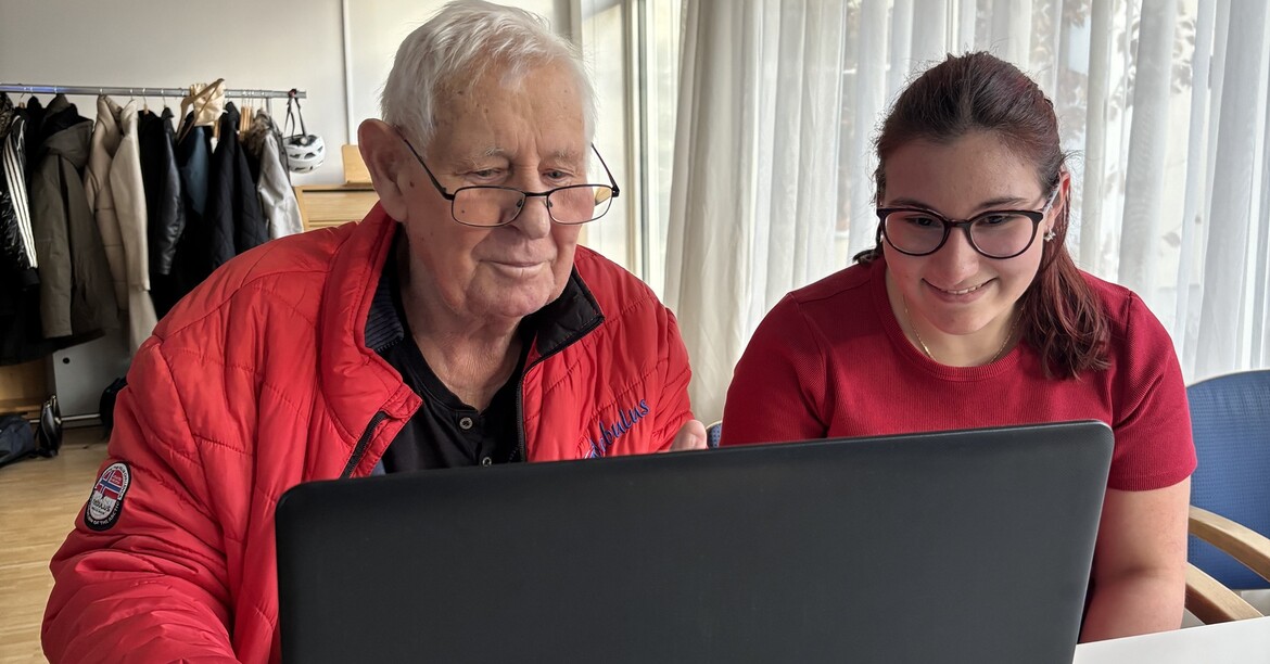Ein älterer Herr und eine Schülerin schauen auf einen Laptop